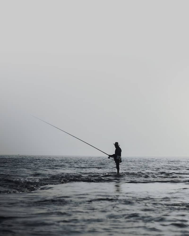 A lone figure fishes in the ocean at dawn.