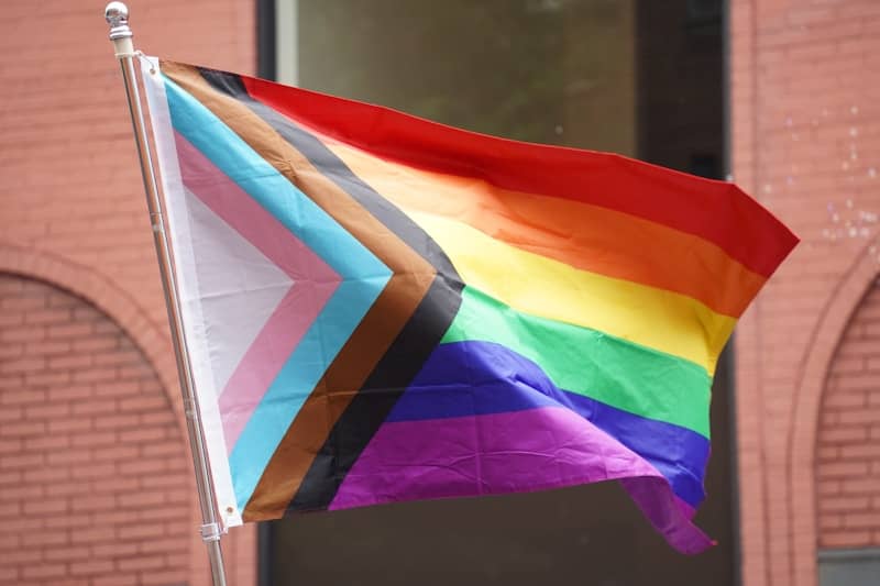 A rainbow colored flag on a pole in front of a building