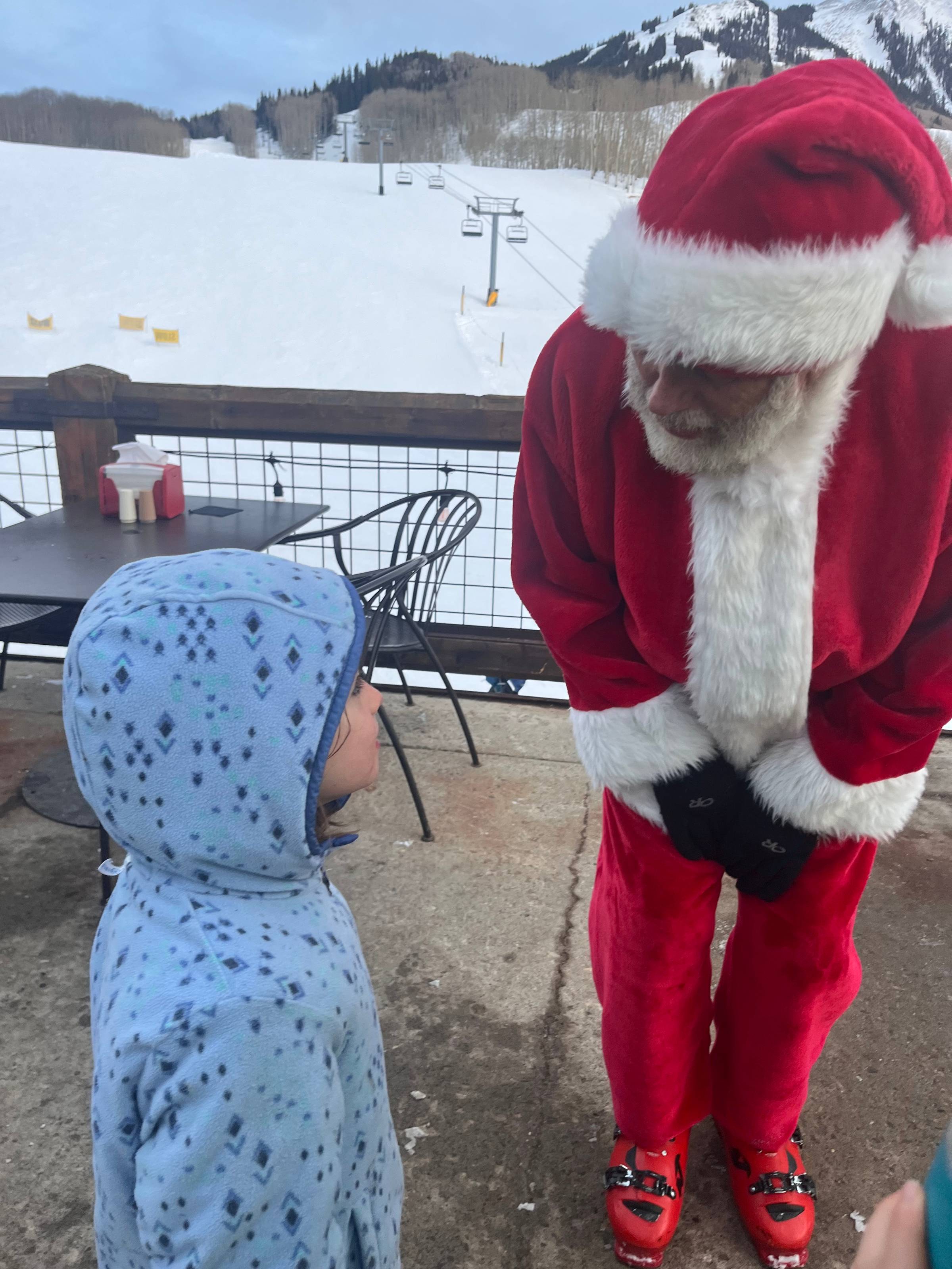 A little girls greets a Santa in ski boots.