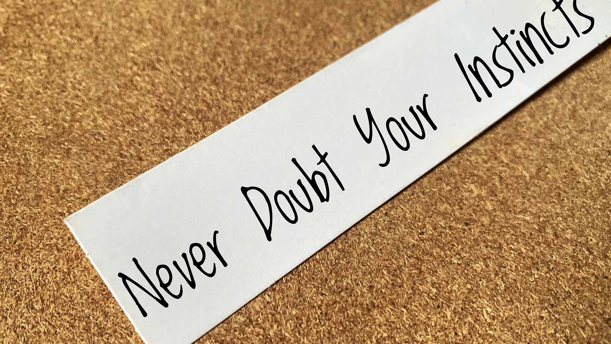 A handwritten note pinned to a corkboard that reads "Never Doubt Your Instincts" — a reminder of the self-authorship that erodes quietly when we consistently outsource our decisions to outside voices before trusting our own judgment.