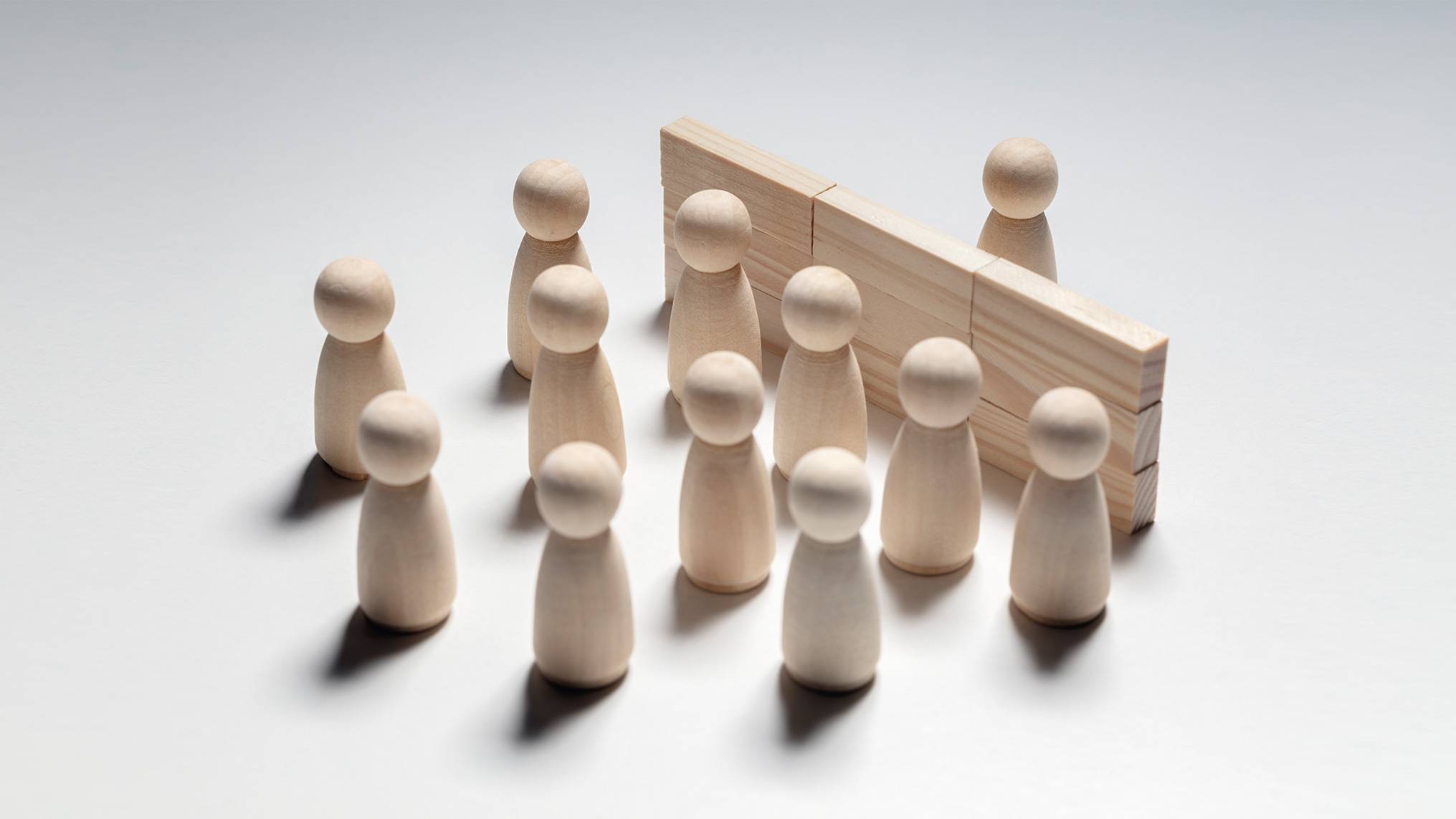 Wooden peg figures arranged in a group, divided by a pair of wooden planks standing upright like a barrier — a visual metaphor for the boundary between healthy empathy and emotional leakage, illustrating how unregulated emotional absorption blurs the line between understanding others and being overtaken by their emotional states.