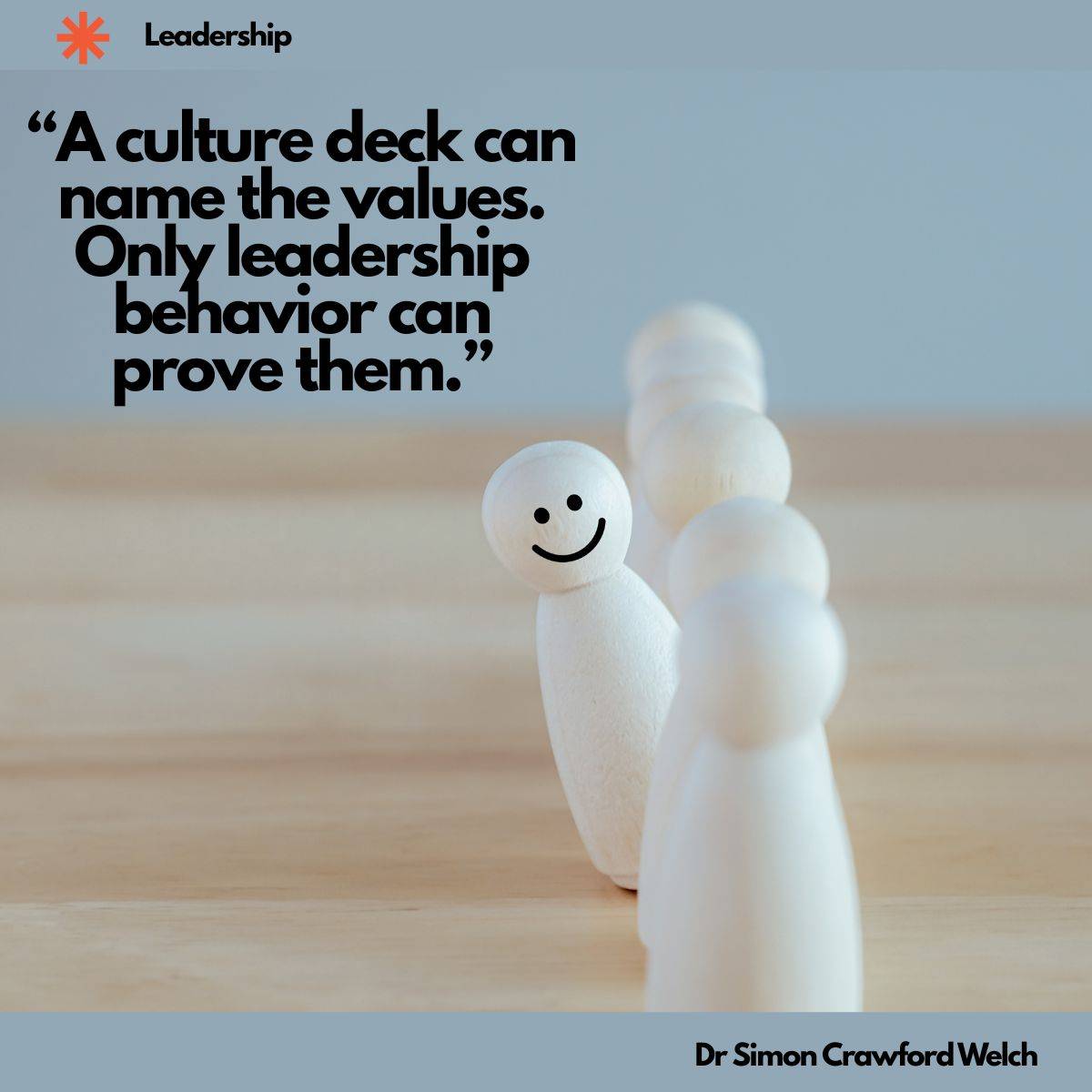 A row of plain wooden peg figures stands on a light wood table, and the one at the front has a smiling face drawn on it while the others behind it are blank, with a Leadership label in the top corner. The image represents a leader whose visible behavior sets the example the rest of the team follows. Quote over the image reads: "A culture deck can name the values. Only leadership behavior can prove them." By Dr. Simon Crawford Welch.