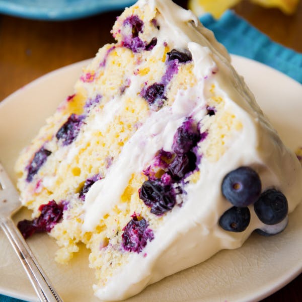 slice of three layer lemon blueberry cake with creamy frosting