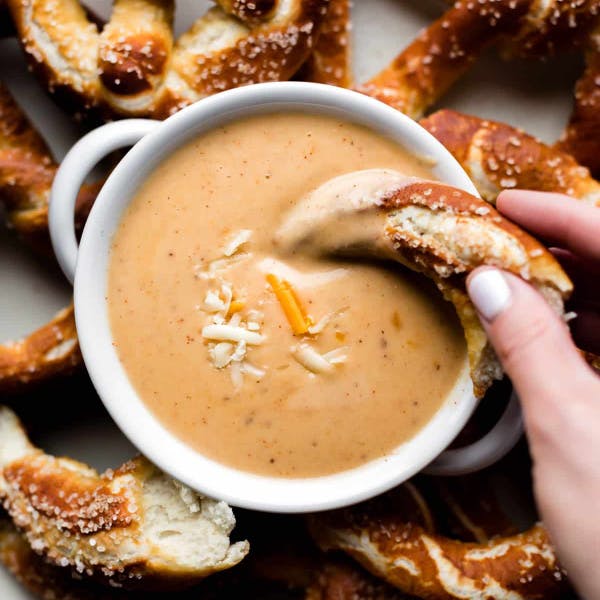 hand dipping a piece of soft pretzel in a bowl of beer cheese dip