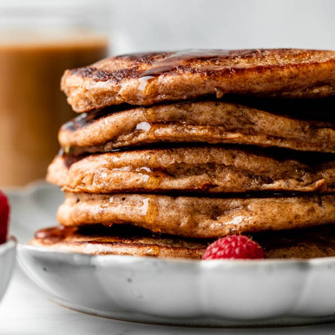 A stack of fluffy whole wheat pancakes on a scalloped white plate