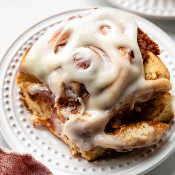 fluffy cinnamon roll on a white plate with thick frosting