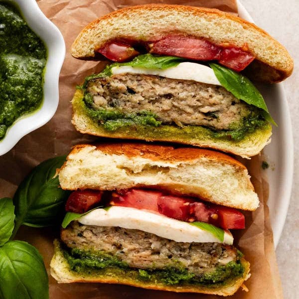 2 caprese chicken burgers on brioche buns with pesto, tomato, mozzarella, and fresh basil