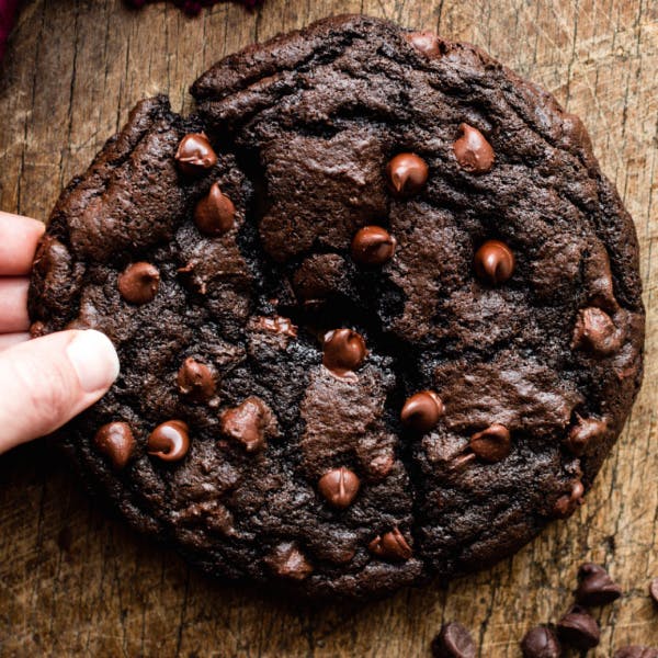 a giant chocolate cookie, broken in half on a wood background