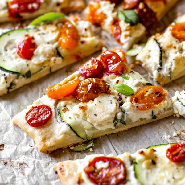 picture of flatbread topped with blistered cherry tomatoes, herbed ricotta, goat cheese, and zucchini