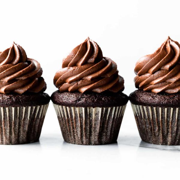 three chocolate cupcakes with whipped ganache piped on top