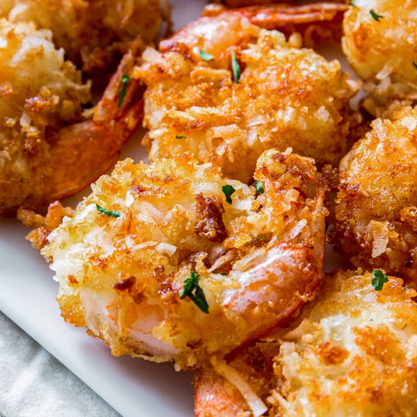 golden coconut shrimp being dipped in spicy-sweet sauce