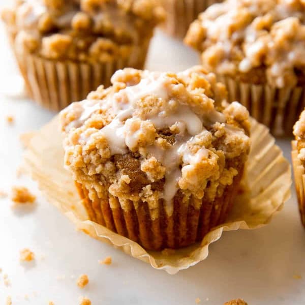 pumpkin crumb cake muffins in wrappers with vanilla icing drizzle