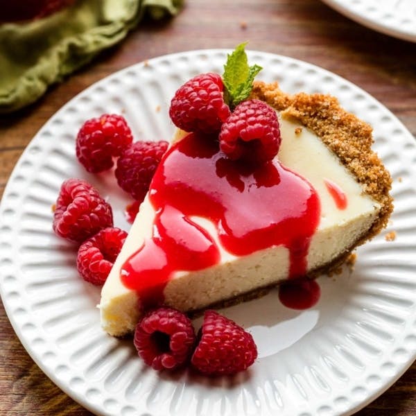 picture of a slice of cheesecake pie on white plate with raspberry sauce