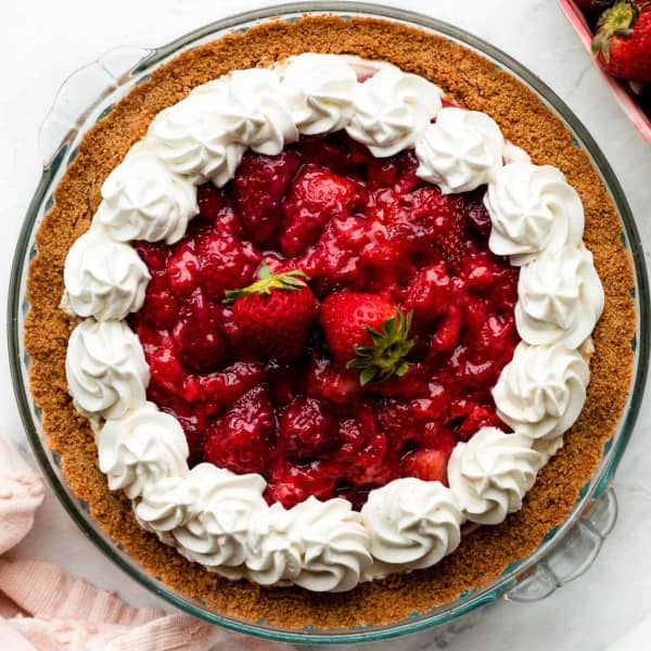 a pie in a glass pie dish, showing strawberries, whipped cream, and graham cracker crust