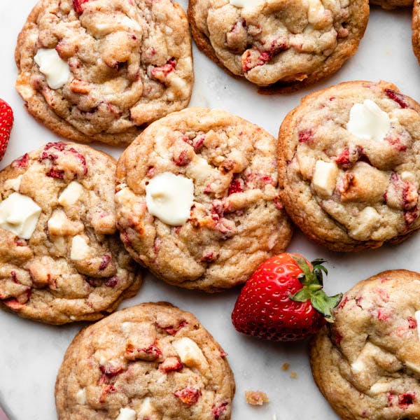 strawberries and cream cookies spread out on a white marble backdrop