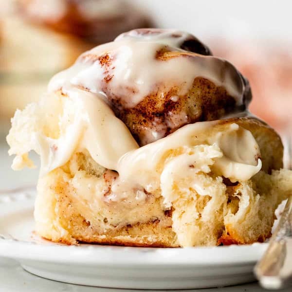 Close up of a fluffy cinnamon roll with icing on a white plate