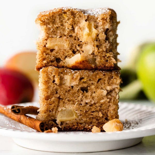 2 square slices of apple cake stacked on a plate and dusted with powdered sugar