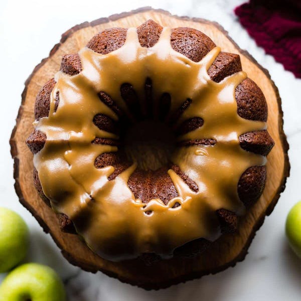 apple bundt cake drizzled with brown sugar glaze on a wooden cake stand 