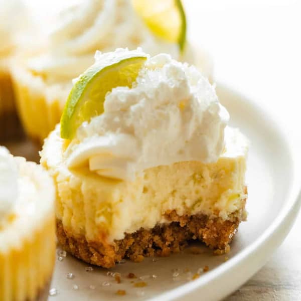 small cheesecake with a bite taken out, topped with whipped cream and a lime