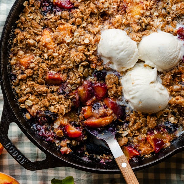 skillet of peach blueberry crisp with vanilla ice cream on top