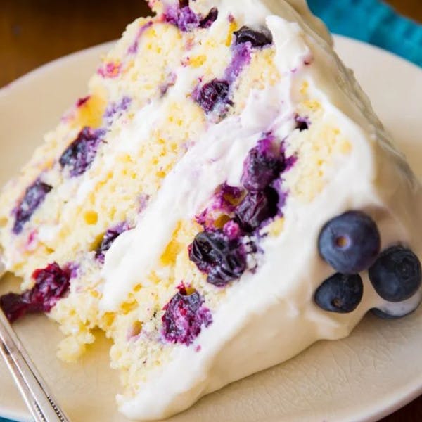 slice of lemon blueberry layer cake on an off-white plate