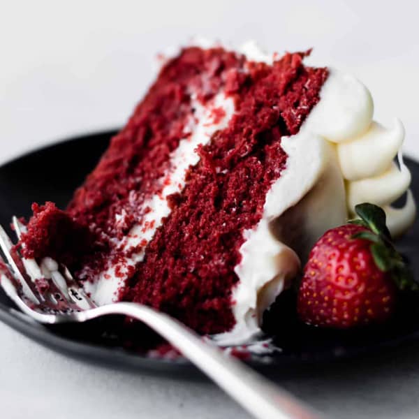 Slice of red velvet cake with cream cheese frosting on a black plate