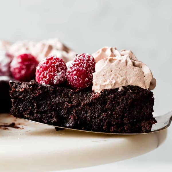 a slice of rich chocolate cake, topped with raspberries and light brown whipped cream