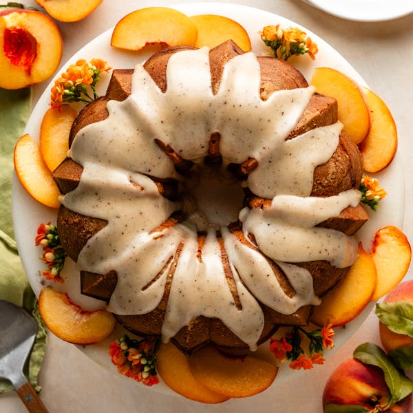 peach bundt cake on a serving stand surrounded by peach slices