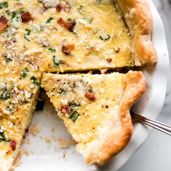 Quiche in a white pie dish, with a slice being removed