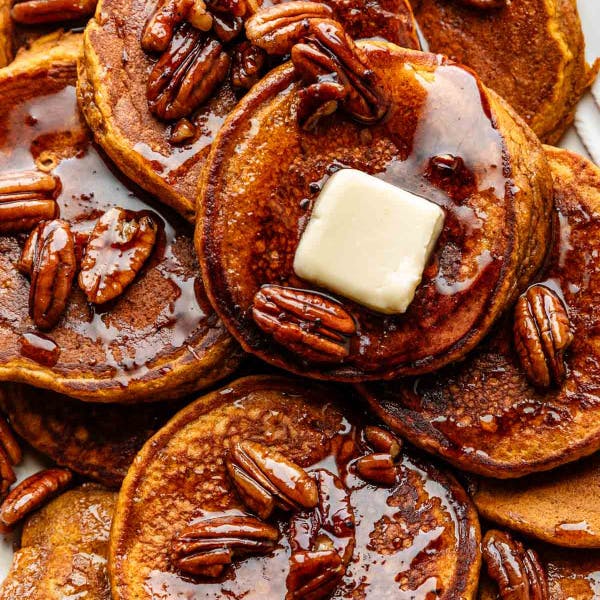 platter of pumpkin pancakes topped with butter pecans and maple syrup