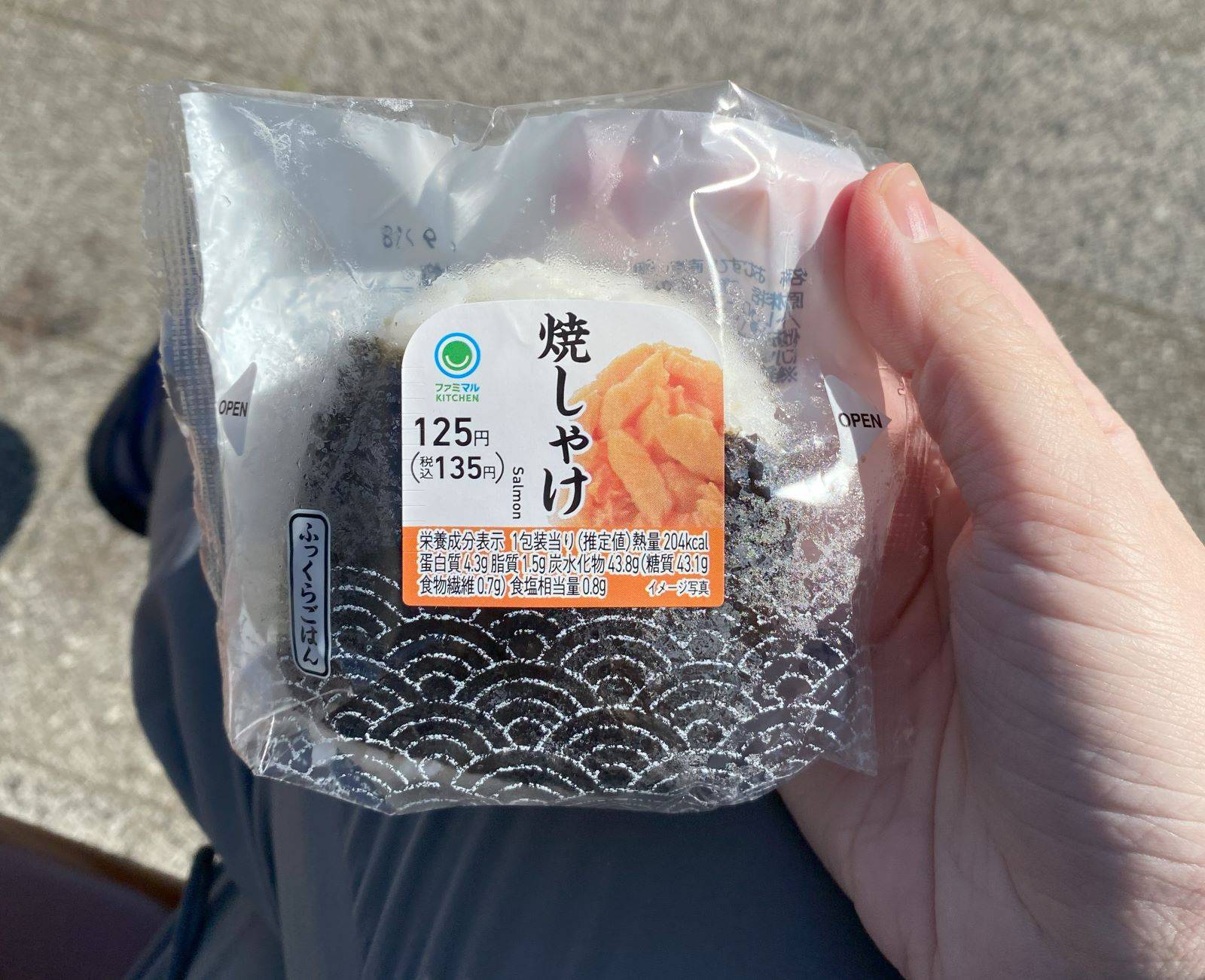 A hand holding a round rice ball inside a plastic wrapper.