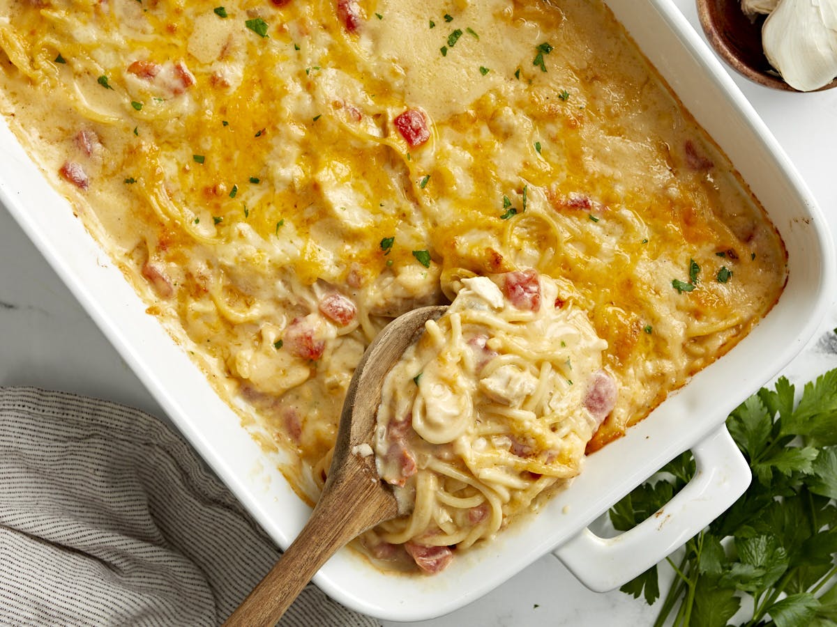 Overhead view of chicken spaghetti in a casserole dish with a wooden spoon scooping some out.