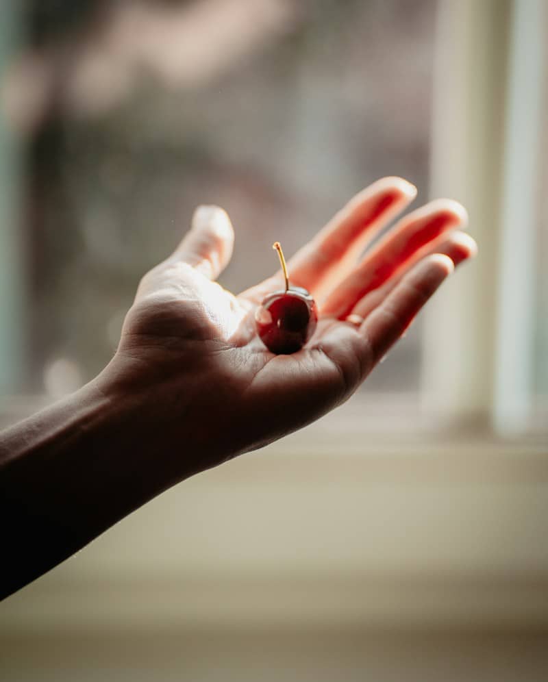 A single red cherry resting in an open palm in soft sunlight