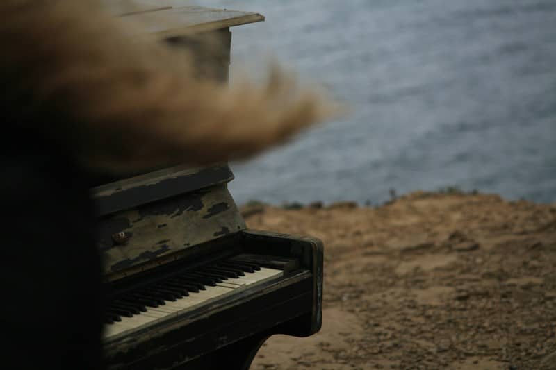 An old upright piano on a rocky cliff overlooking the sea with blurred hair in the foreground