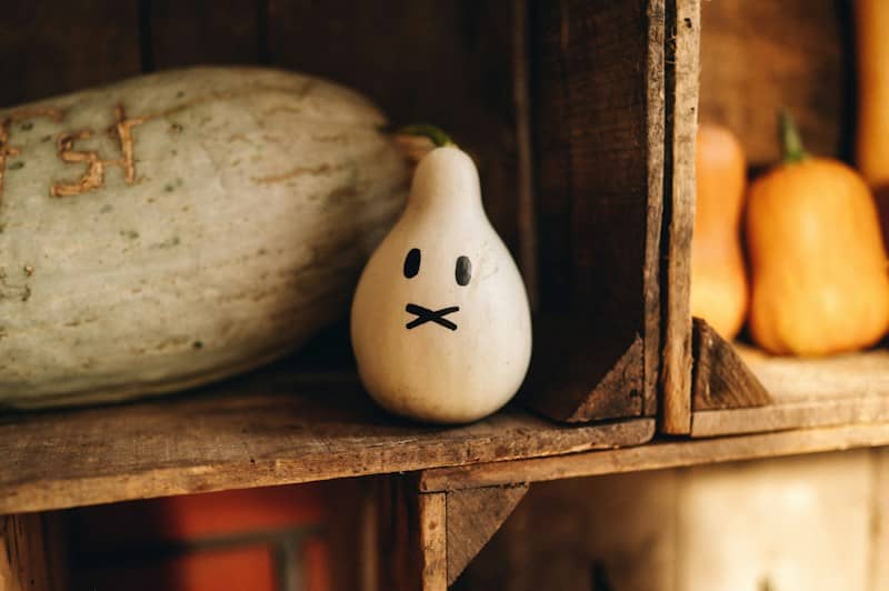 A small white gourd with a painted face on a rustic wooden shelf