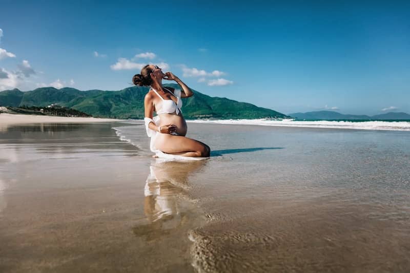 Pregnant woman posing on a wet sandy beach.
