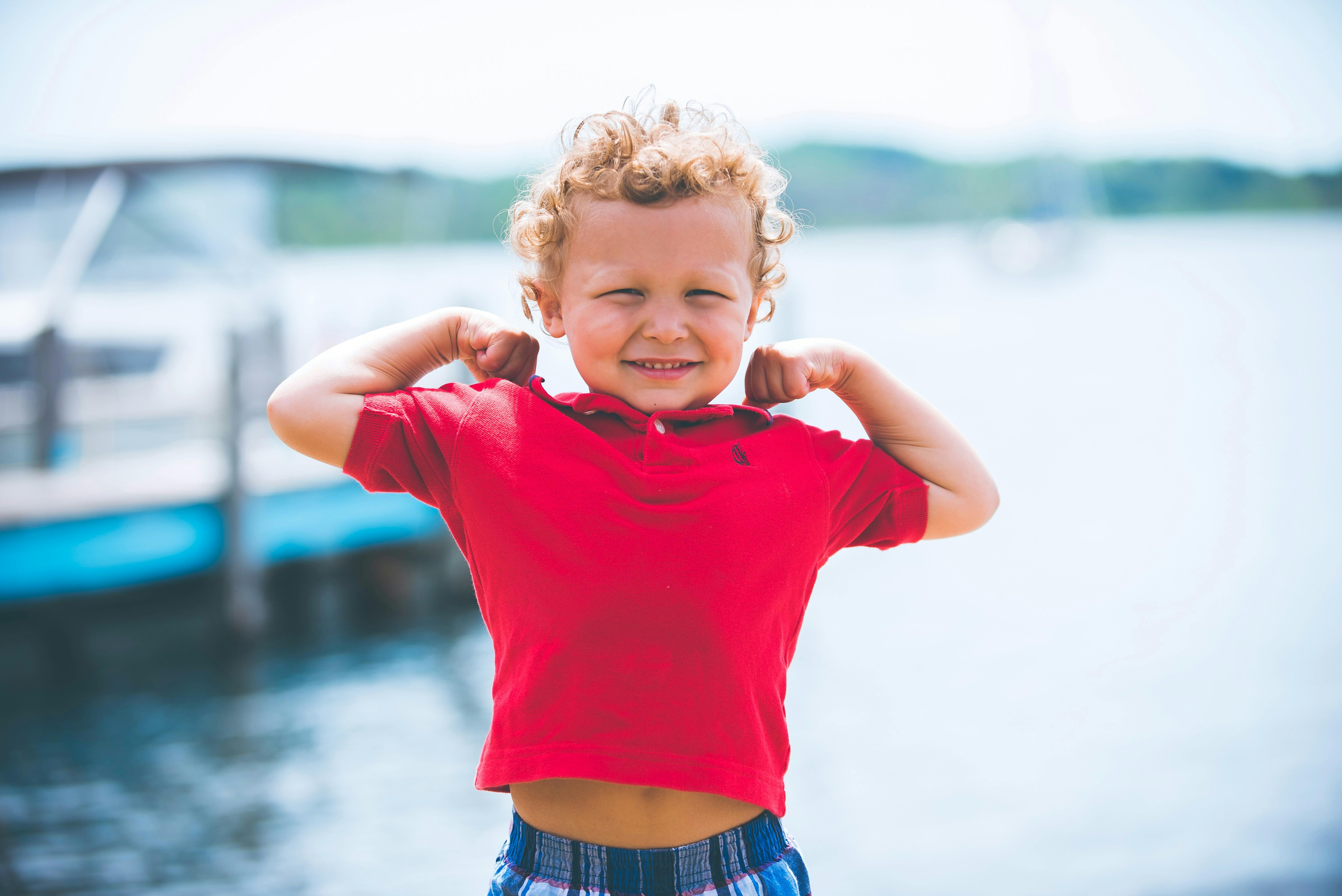 Healthy happy kid on dock on lake flexing his biceps