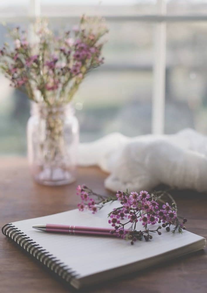 shallow focus photo of purple flowers on white spiral notebook