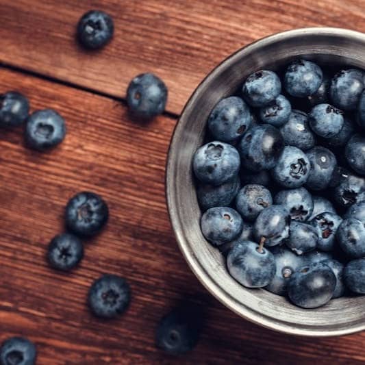 A metal bowl filled with blueberries on top of a wooden table