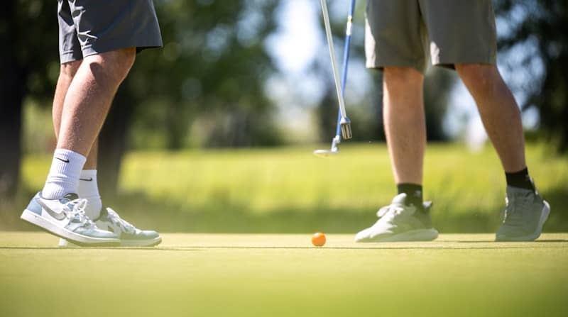 Golfers' legs and an orange ball on a putting green.