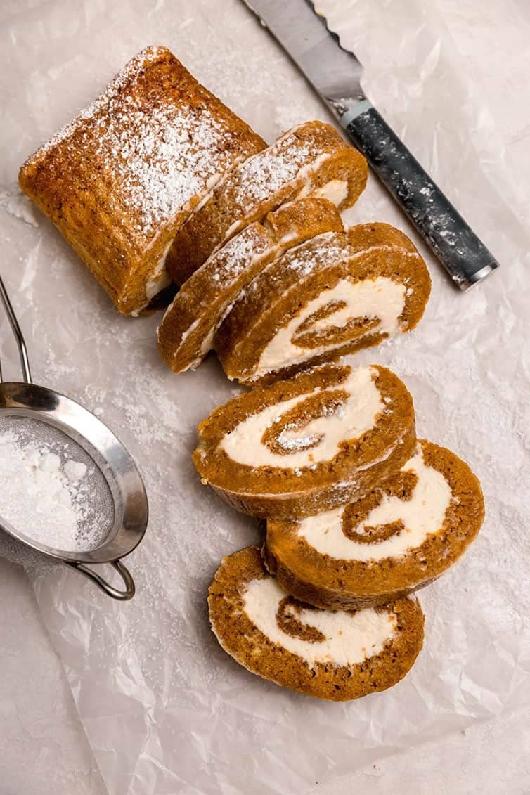 Overhead image of a sliced pumpkin roll on parchment paper.