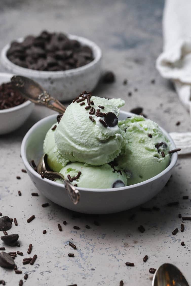scoops of mint chocolate chip ice cream in a white bowl with spoons