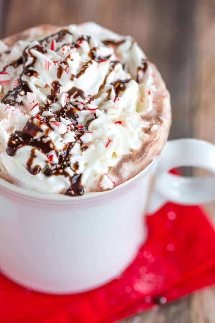 hot chocolate in a white mug topped with whipped cream, chocolate drizzle, and crushed peppermint