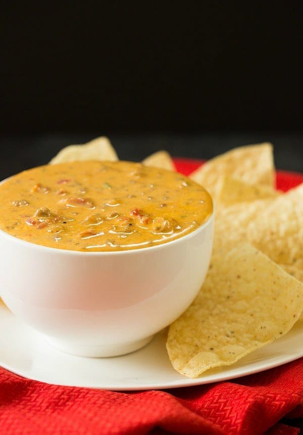 Queso in a white bowl surrounded by tortilla chips.