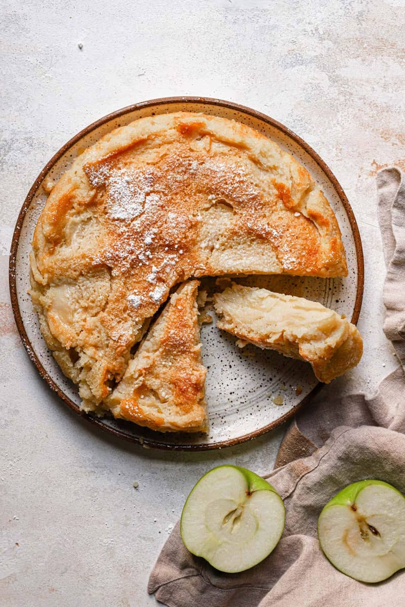 overhead image of French apple cake on a white plate with a few slices removed
