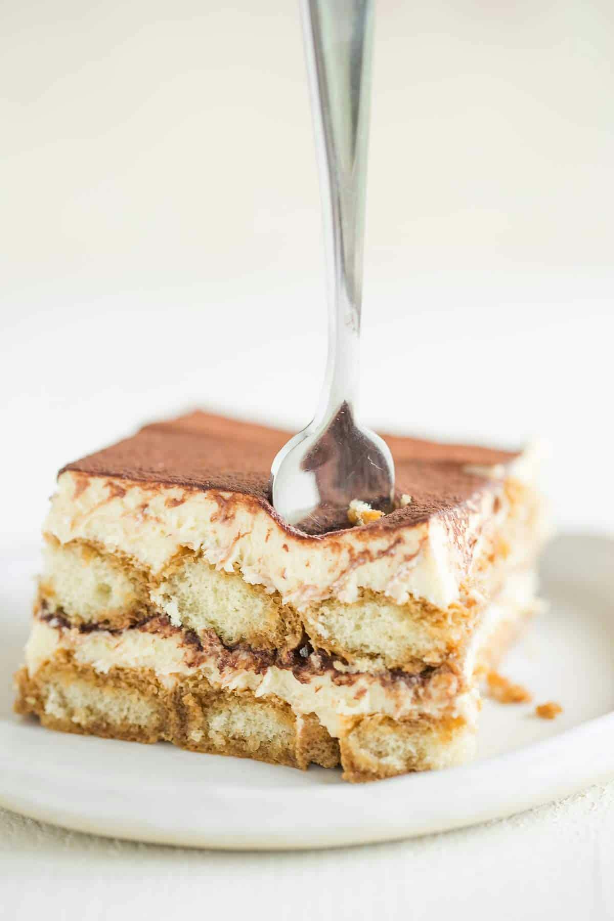 a serving of tiramisu on a white plate with a spoon stuck in it