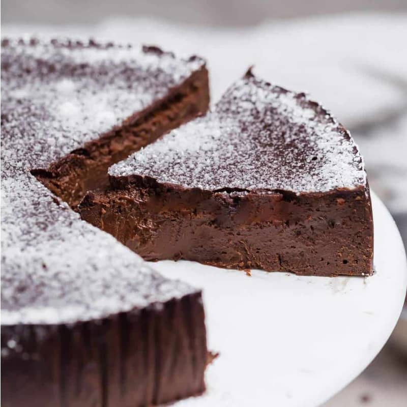 Flourless chocolate cake on a white cake stand with a slice showing.