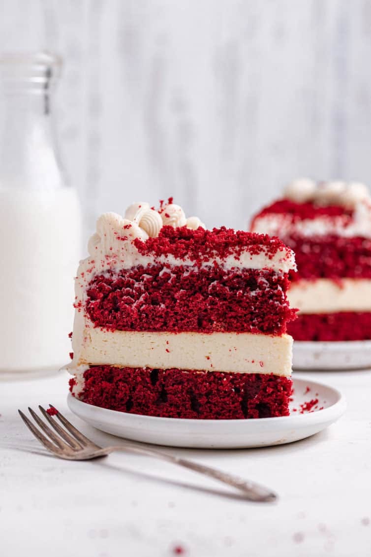 side view of a slice of layered red velvet cheesecake on a white plate
