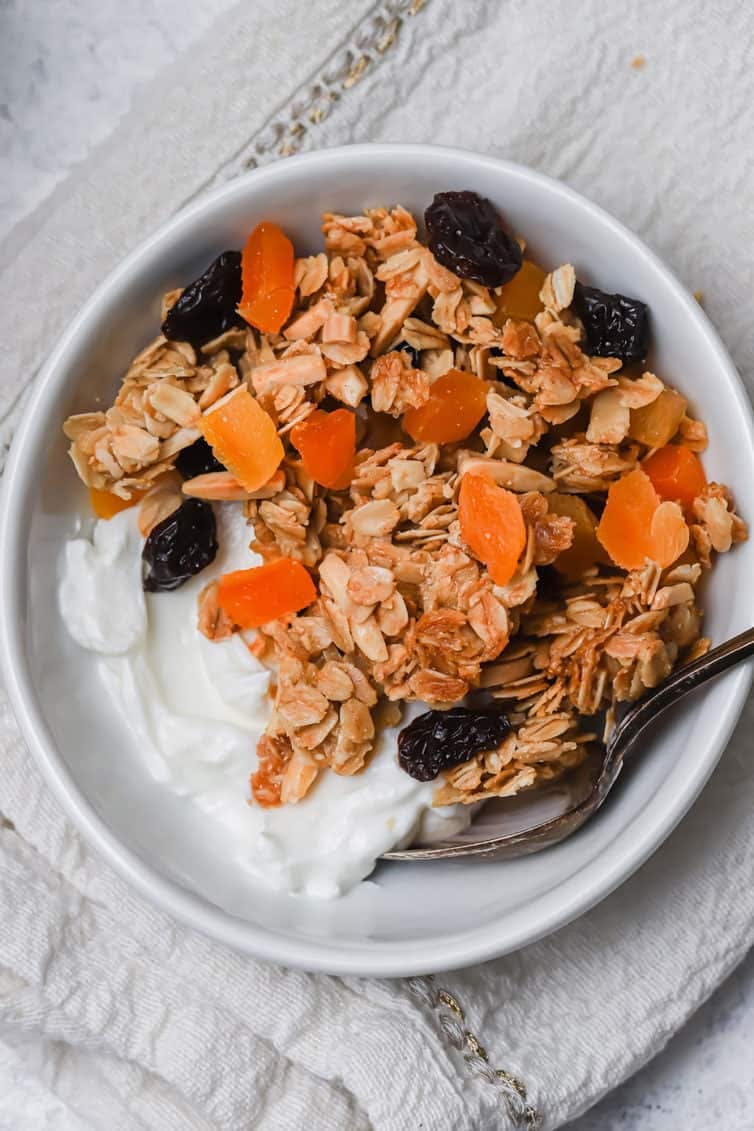 overhead image of granola on top of yogurt in a white bowl with a spoon