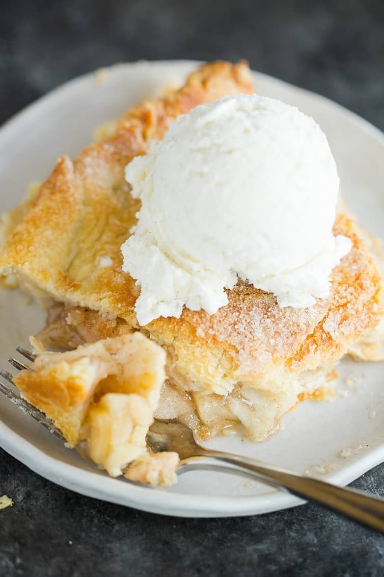 Slice of apple pie topped with a scoop of vanilla ice cream on a white plate with a fork.